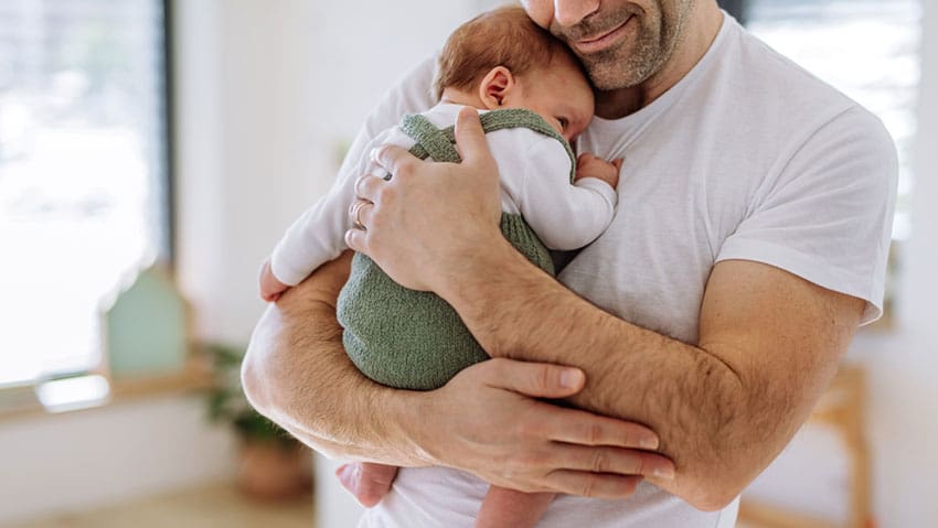 Stock photo of a father holding a baby, illustrating the economic and social benefits of paid paternity leave