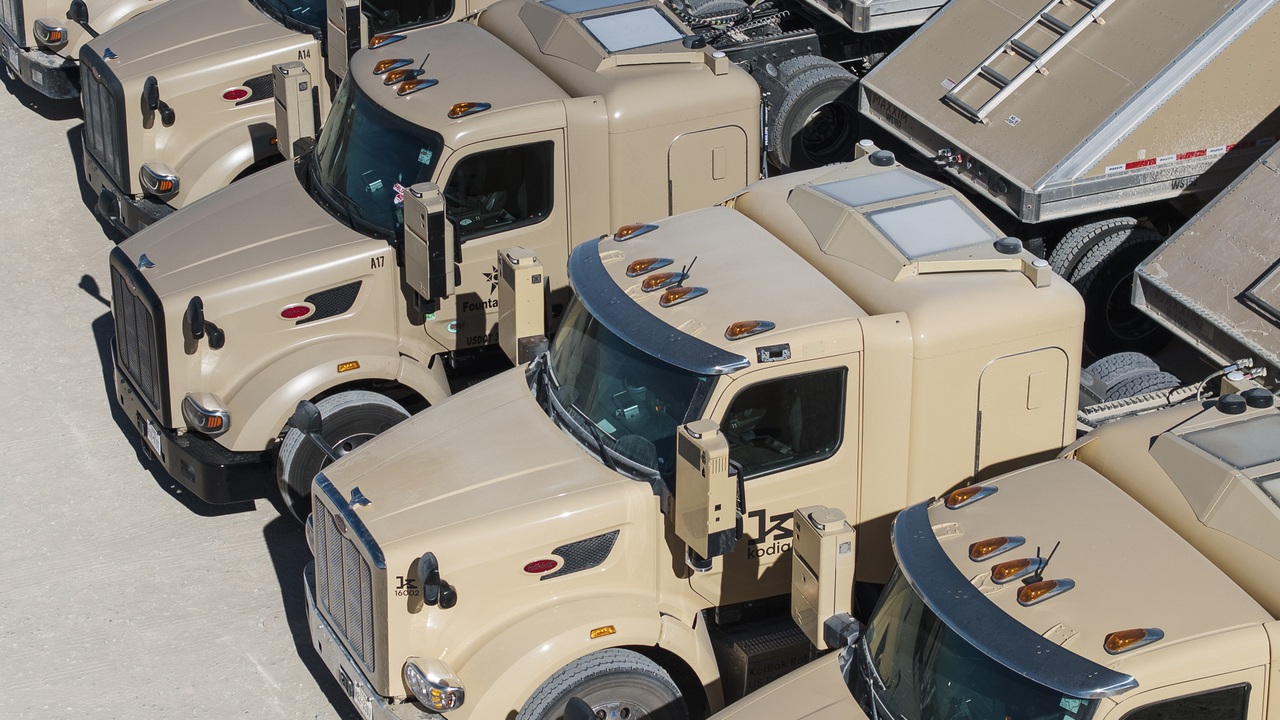 Beige Kodiak autonomous semi-trucks with roof-mounted sensor pods parked in an outdoor lot