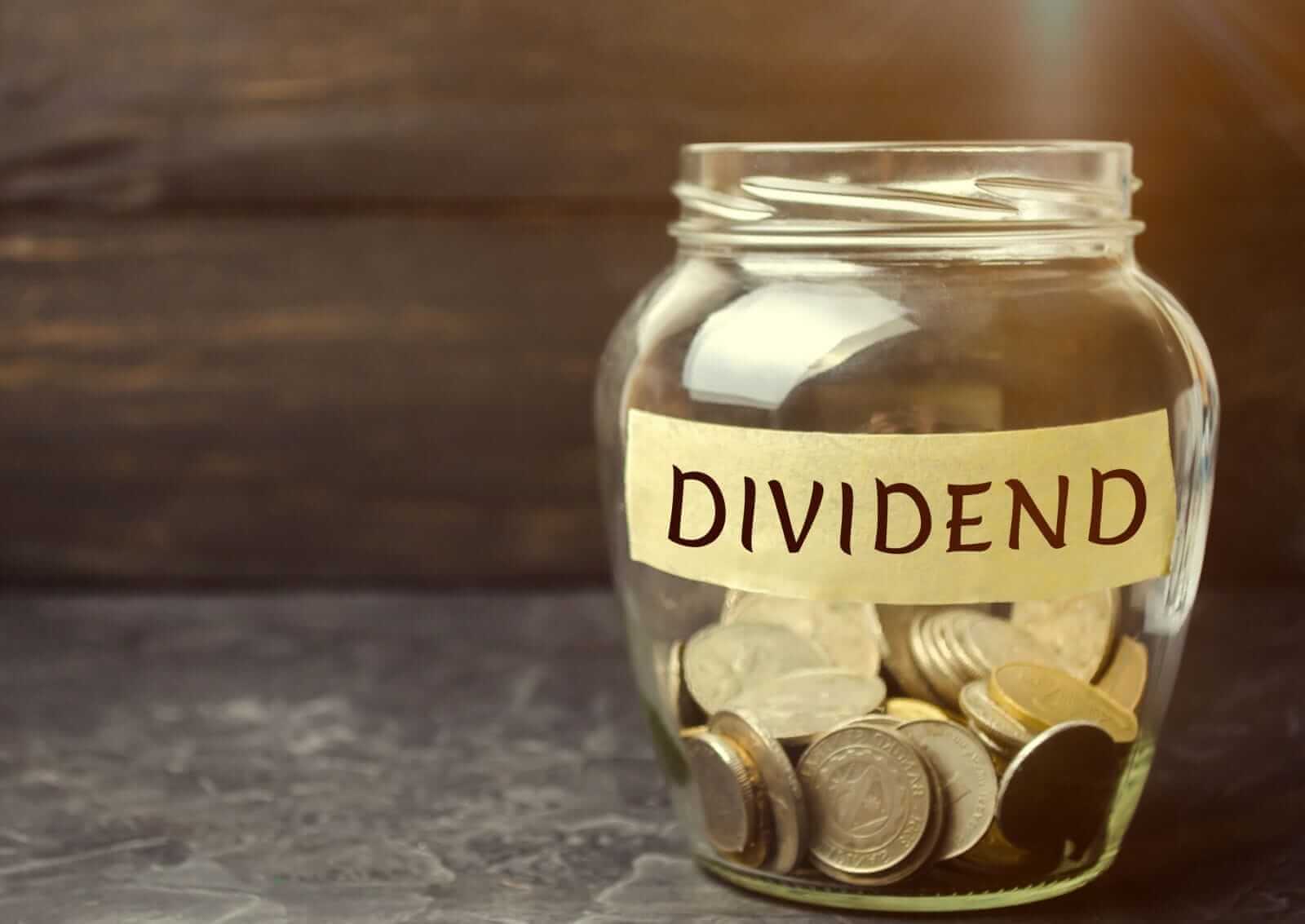 Glass jar labeled "Dividend" with financial charts and pen
