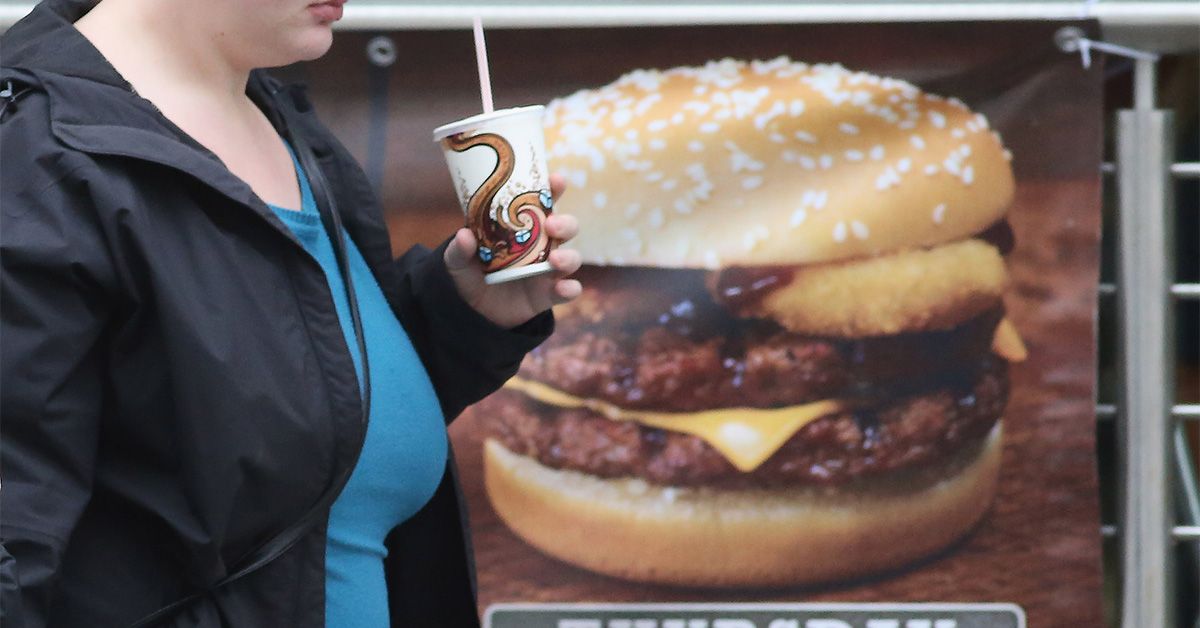 Person walking past a burger sign — ultra-processed food impact on health