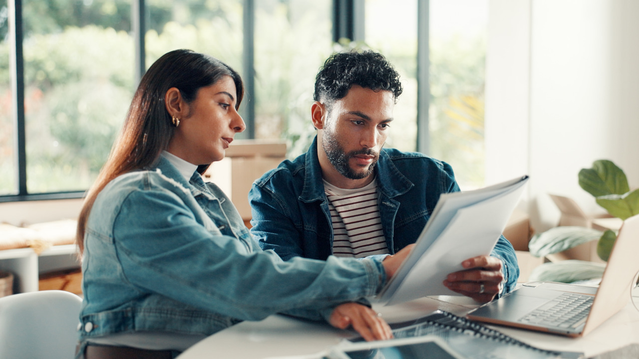Descriptive caption: A person reviewing financial documents and a laptop screen showing budget charts, illustrating the September financial checkup