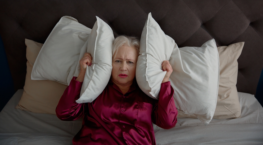 Elderly woman suffering from noise, trying to sleep in bed — illustrating sleep disruption linked to menopause symptoms