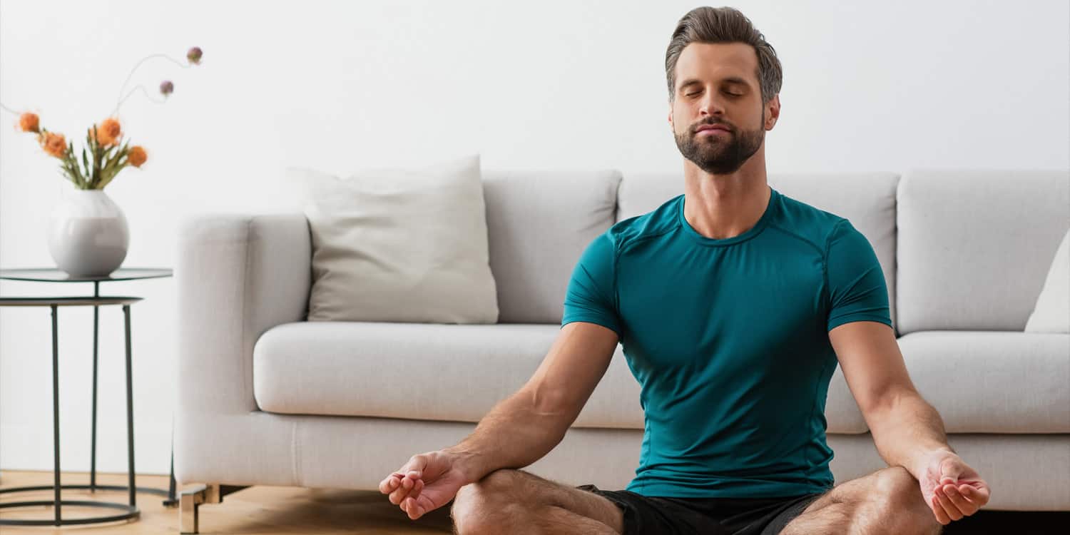 Man with closed eyes meditating in lotus pose on yoga mat