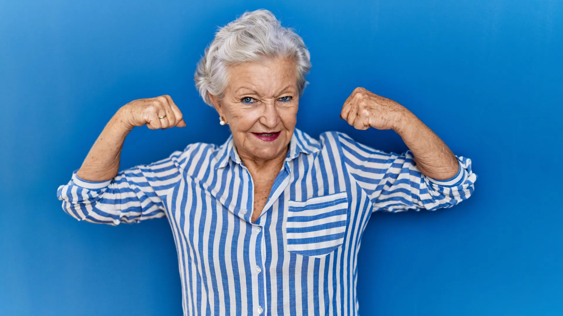 Senior woman flexing muscles to demonstrate strength testing