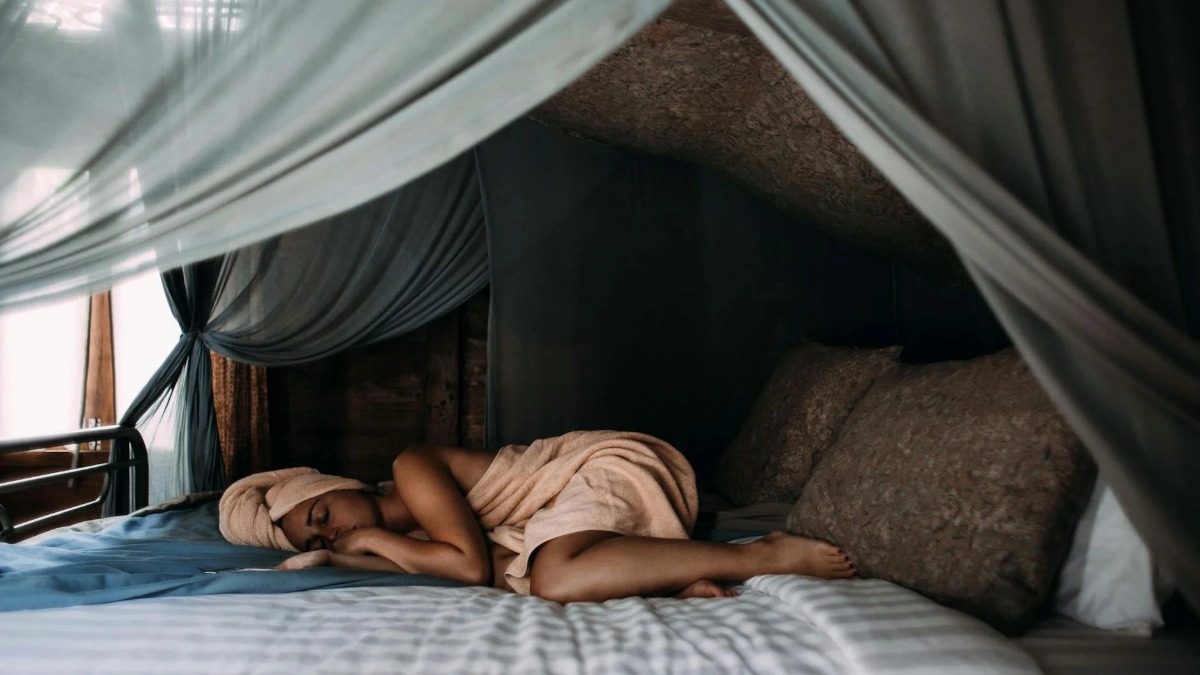 A woman resting peacefully on a canopy bed at a tranquil sleep retreat, representing the growing sleep tourism trend